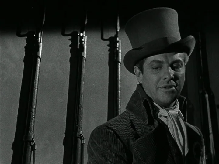 The Black Book (Reign of Terror) (1949) movie still: medium — A dimly lit room features a row of rifles mounted on the wall. A man wearing a top hat…
