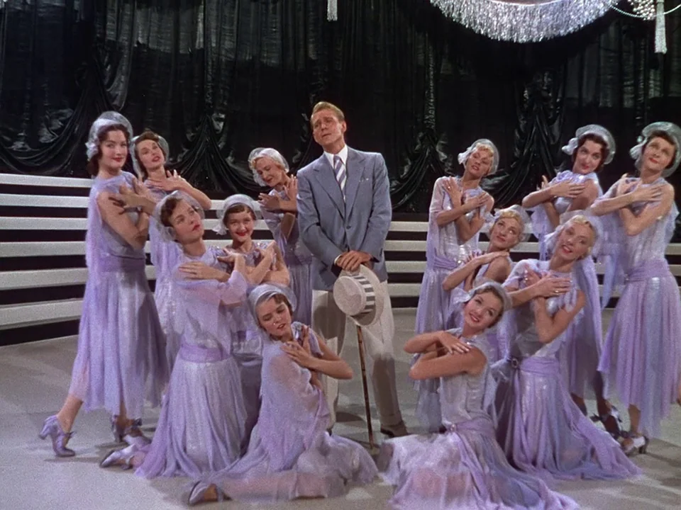 Singin’ in the Rain (1952) movie still: fullbody — A theatrical stage setup features a male performer surrounded by several dancing women. The…