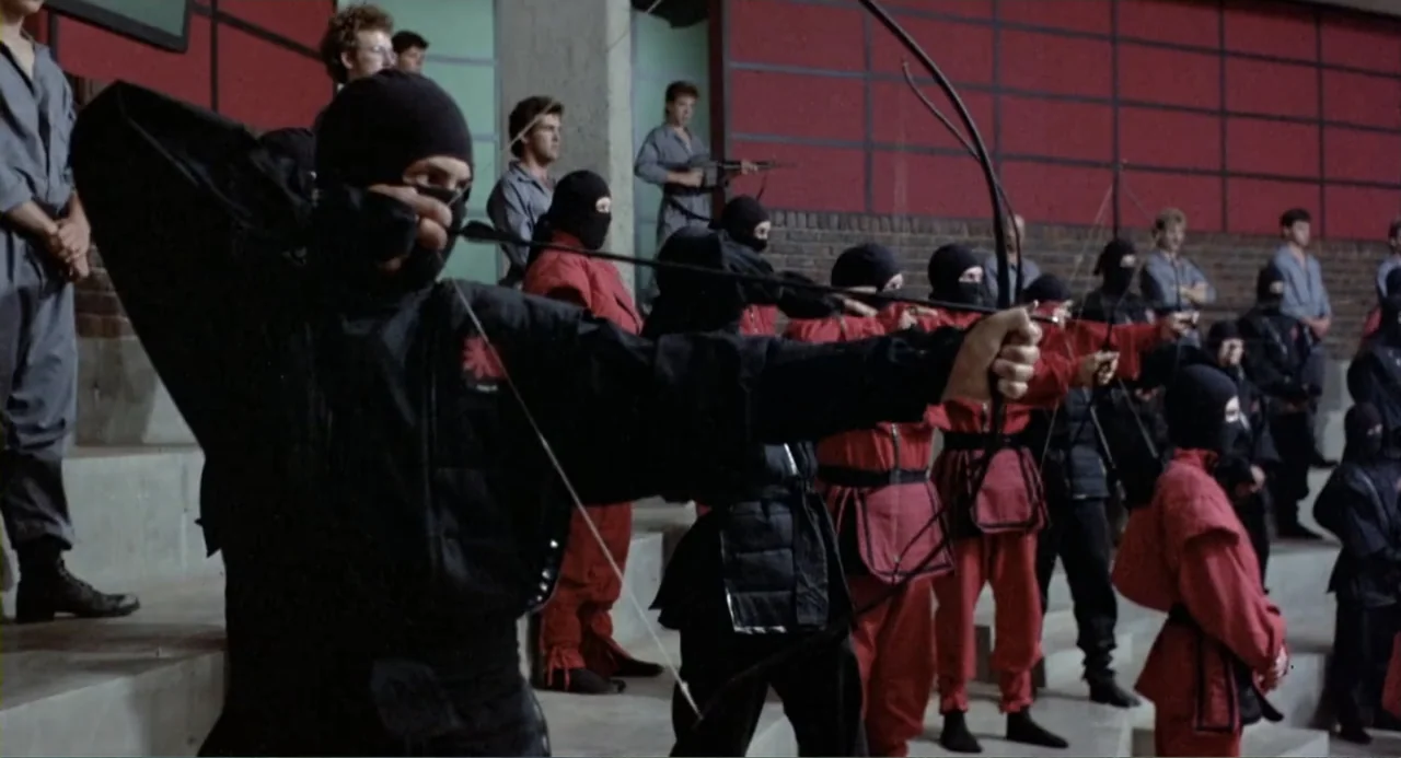 American Ninja 2: The Confrontation (1987) movie still: medium — A group of people dressed in ninja uniforms stand on indoor concrete bleachers. One…