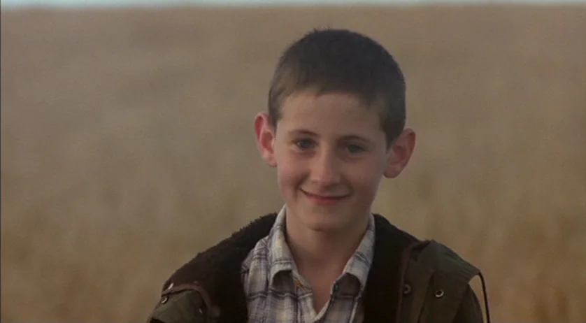 Ratcatcher (1999) movie still: medium — A boy stands in a vast, hazy agricultural field filled with dry golden stalks. The child stares at the lens…