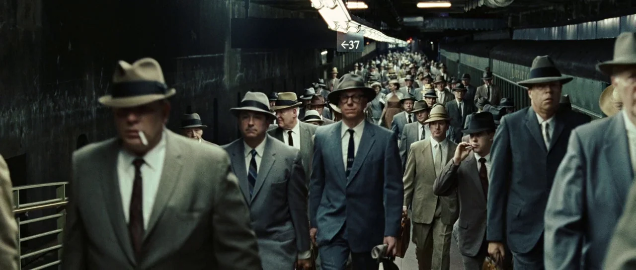 Revolutionary Road (2008) movie still: wide — A dense crowd of men in matching mid-century suits walks along a train platform. The industrial space…