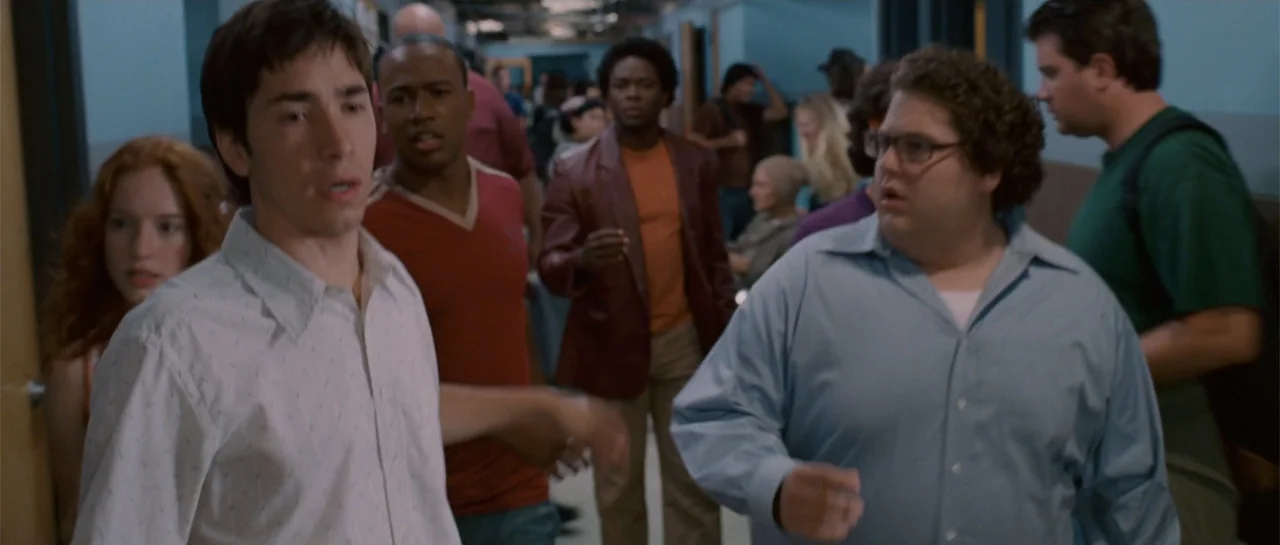 Accepted (2006) movie still: medium — A busy school hallway with blue-painted walls and multiple students walking past each other. Three young men…