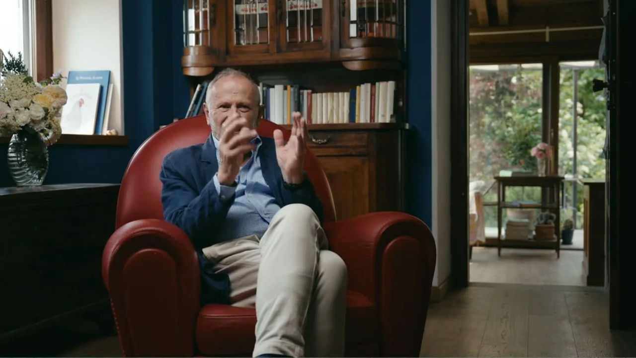 FRAGILE - The story of Nicolò Fagioli (2024) movie still: medium — A living room features dark blue walls, a wooden hutch, and a red armchair. An…