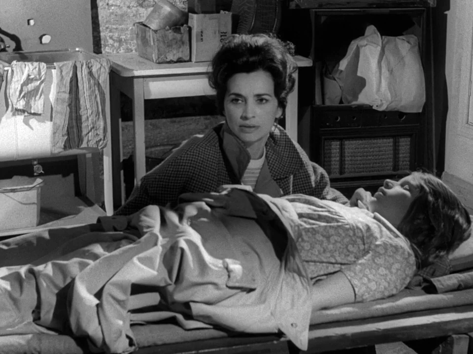 Night of the Living Dead (1968) movie still: medium — A cramped indoor space contains a wooden cot and a washbasin with hanging rags. A woman in a…