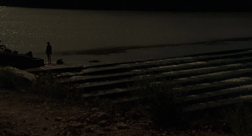 Furia (1999) movie still: wide — A dark, concrete weir structure crosses a body of water at night. A lone figure stands near the edge of the stone…