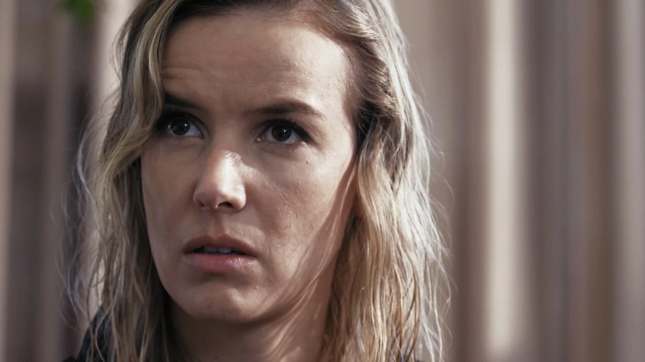 Zero Tolerance (2015) movie still: closeup — An interior space with a beige curtain background provides a simple backdrop. A woman looks off-camera…