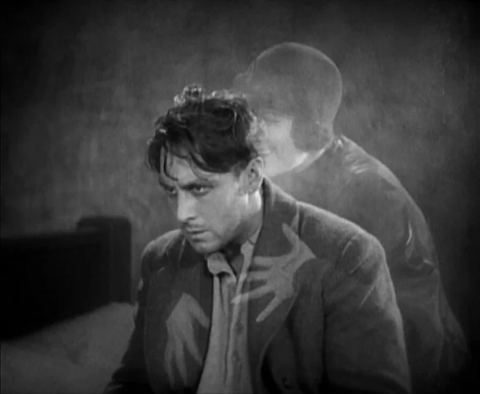 Sunrise (1927) movie still: medium — A dark, dimly lit room contains a man seated in the foreground. A ghostly, transparent apparition of a woman is…