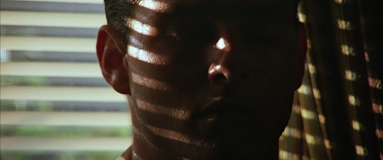 Top Gun (1986) movie still: closeup — An interior space is illuminated by bright sun rays streaming through closed venetian blinds. A man's face is…