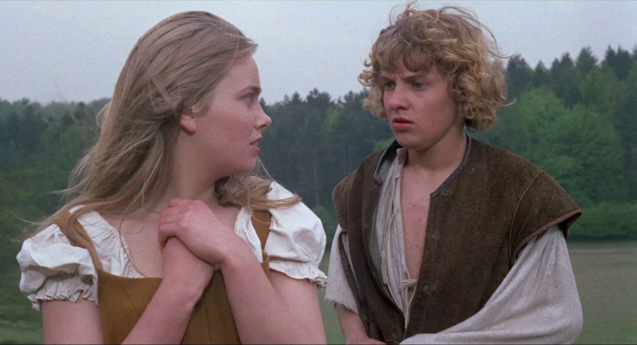 The Blood on Satan’s Claw (1971) movie still: medium — A green, tree-lined meadow provides a background for two adolescents during the day. The girl…