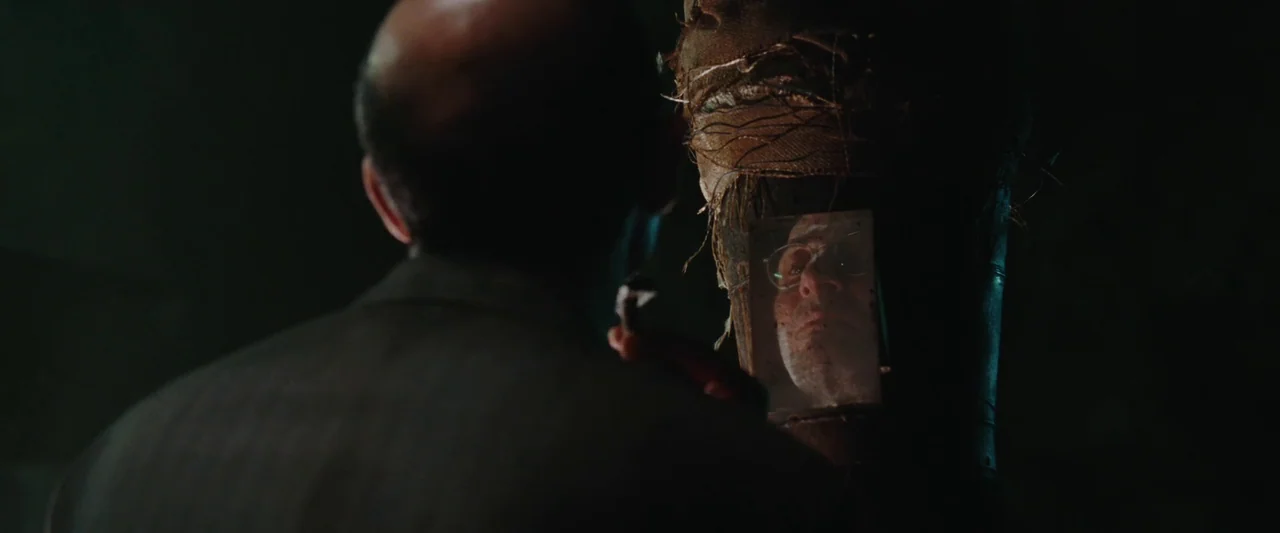 Iron Man (2008) movie still: medium — A dimly lit industrial basement with shadows cloaking the surrounding environment. A man stands facing a…