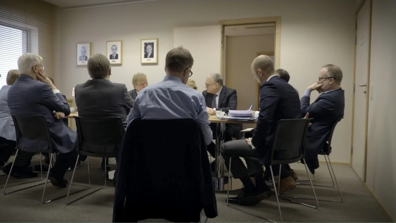 Brexit: Behind Closed Doors (2019) movie still: medium — A small office space contains several men seated around a central table for discussion.…