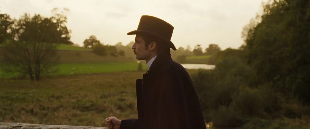 Far from the Madding Crowd (2015) movie still: medium — A rural landscape at golden hour with rolling hills and a distant stream. A man in a period…