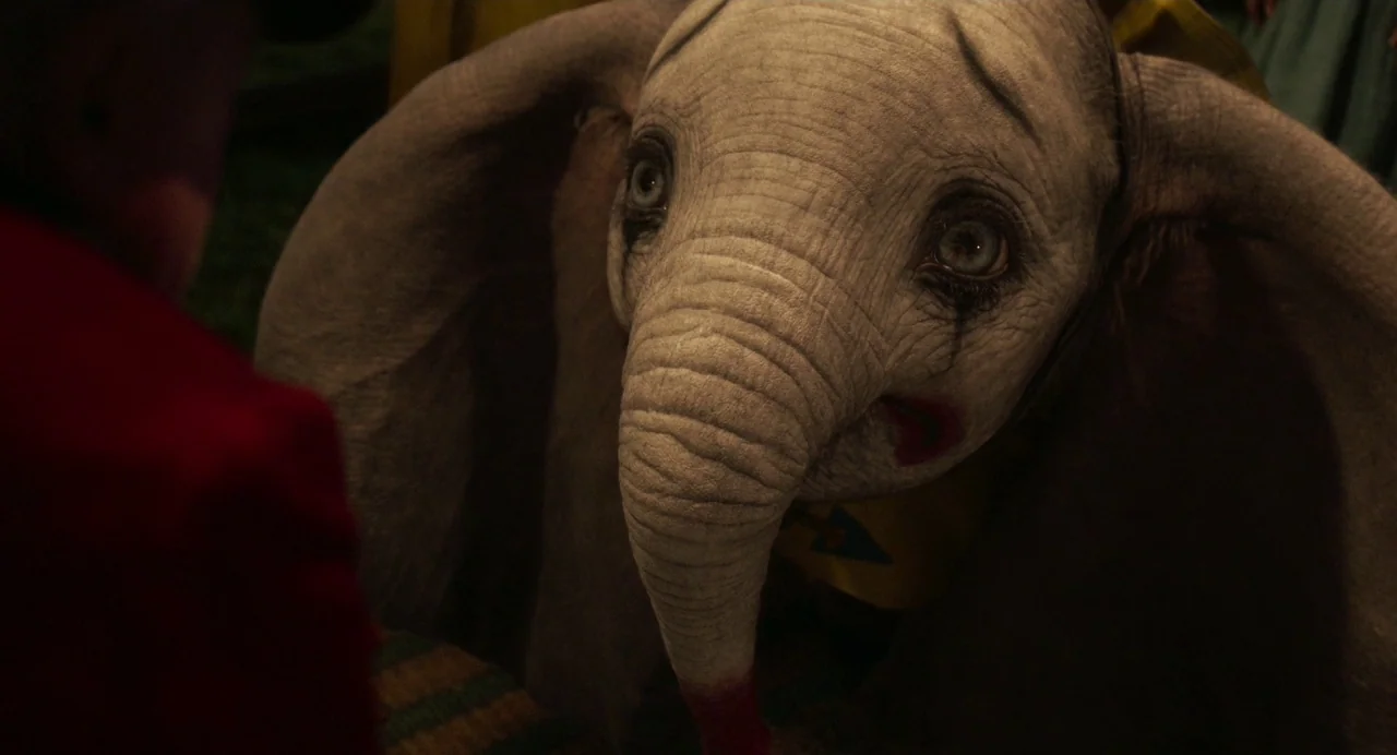 Dumbo (2019) movie still: closeup — A dimly lit circus environment with textured elephant skin visible in close detail. An elephant with smeared red…