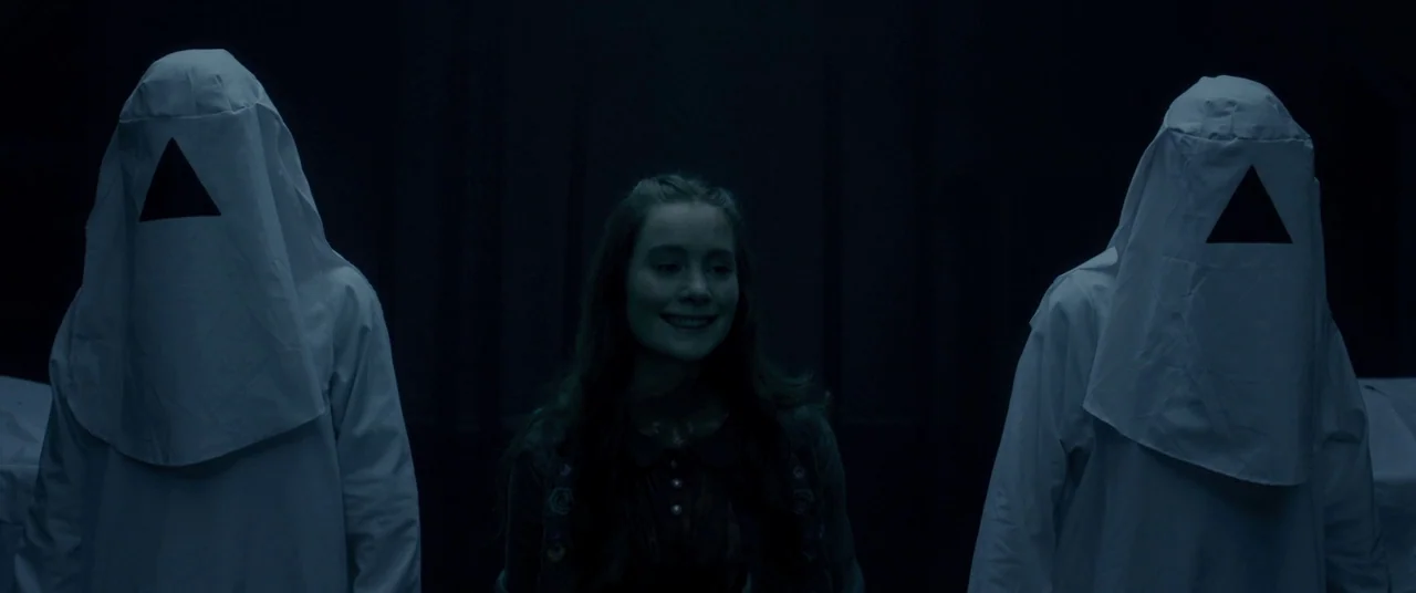 The Void (2016) movie still: medium — A dark, dimly lit room contains three people centered in the frame. A young woman stands between two figures…