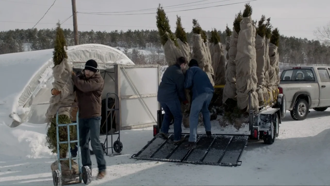 The Captive (2014) movie still: wide — A snowy outdoor nursery yard contains a hoop house and a utility trailer. Three men in work clothes load…