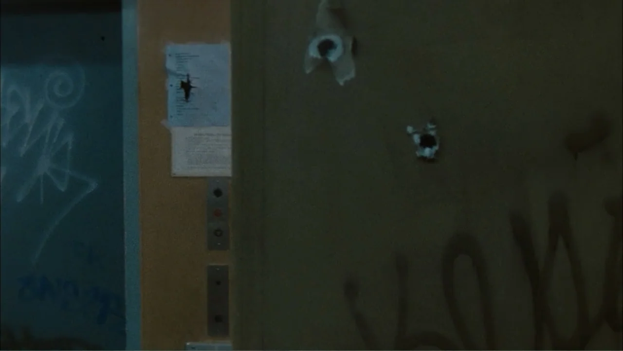 Driven to Kill (2009) movie still: medium — A dark elevator lobby wall contains several bullet holes and graffiti marks. A silver control panel sits…