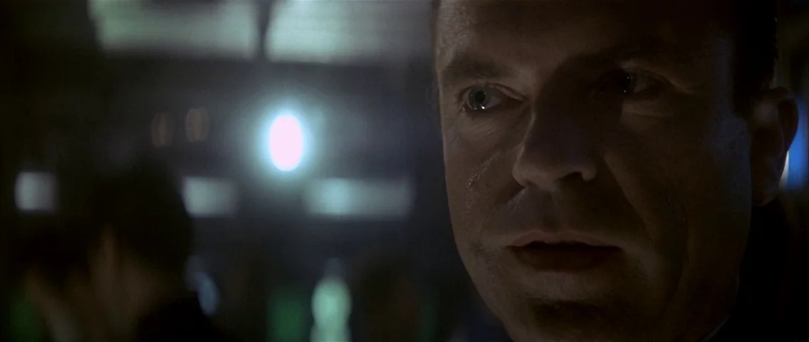 The Hunt for Red October (1990) movie still: closeup — A dark, dimly lit environment with out-of-focus light sources visible in the background. A…
