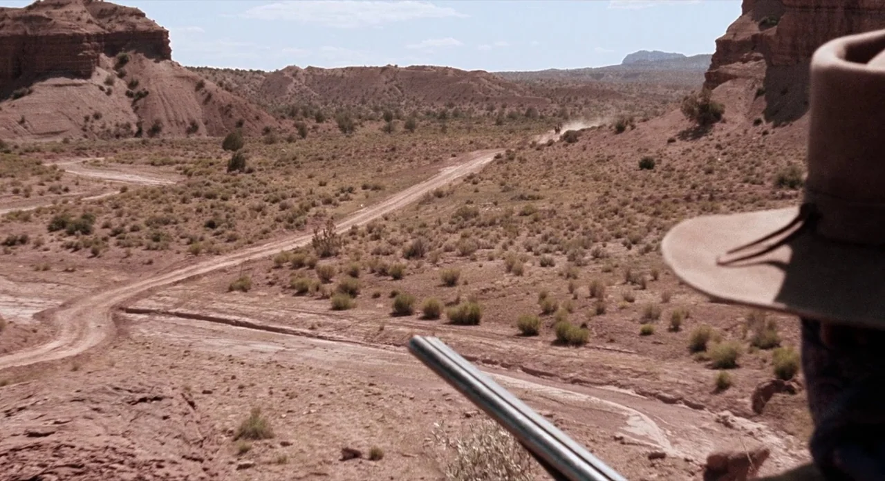 Ride In The Whirlwind (1966) movie still: wide — A vast arid desert canyon with a dirt path winding through scrub brush. The view is from an…