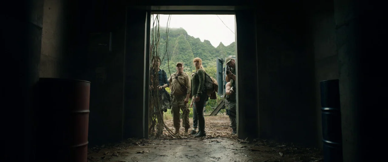 Jurassic World: Fallen Kingdom (2018) movie still: fullbody — A dark concrete bunker entrance is framed by hanging vines and debris. A group of…