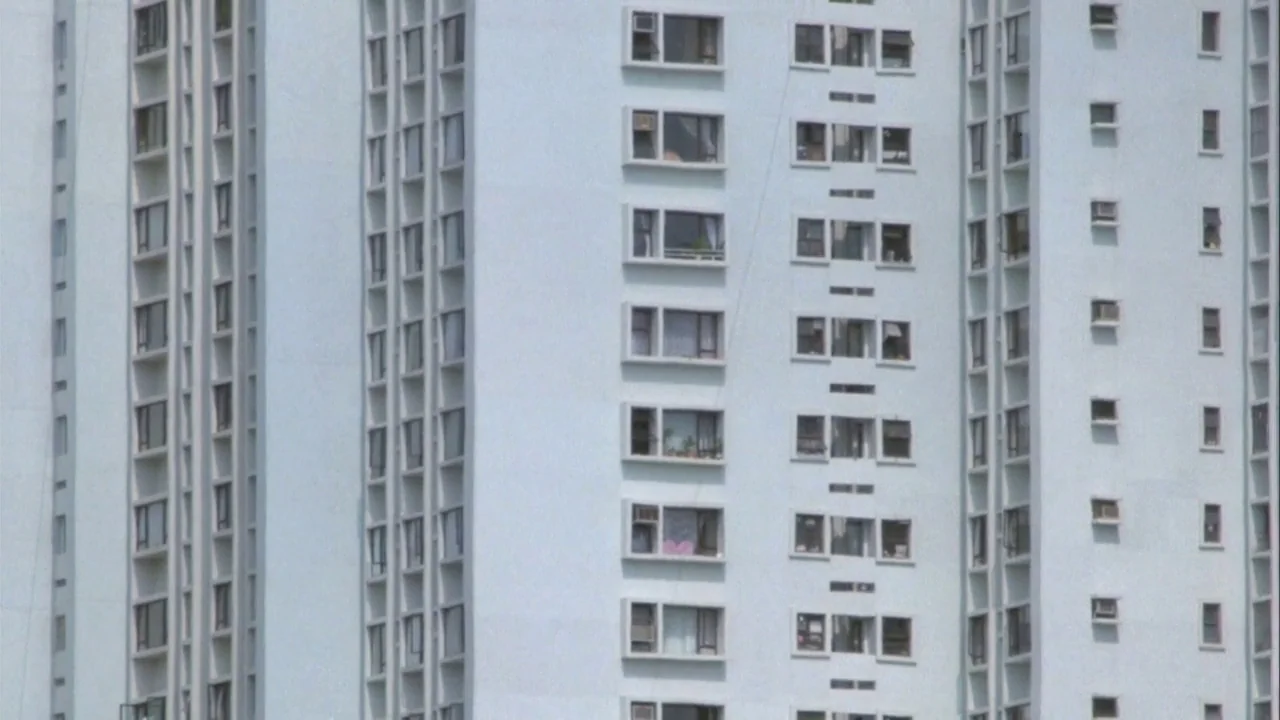 Powaqqatsi (1988) movie still: establishing — A tall, monolithic white apartment building features repeating rectangular windows and recessed…