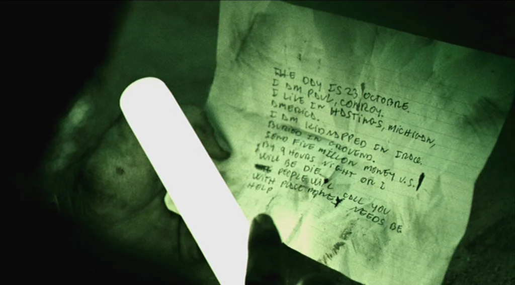 Buried (2010) movie still: closeup — A dark, cramped, and enclosed underground space lit by a singular glowing light stick. A handwritten ransom…