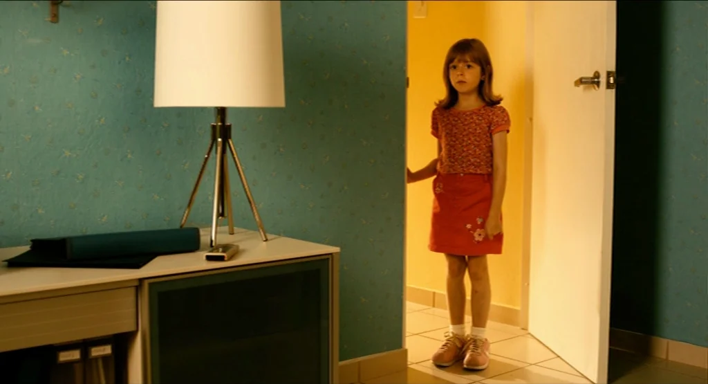 Life During Wartime (2009) movie still: medium — A turquoise-walled room with a desk in the foreground features an open doorway. A young girl in a…