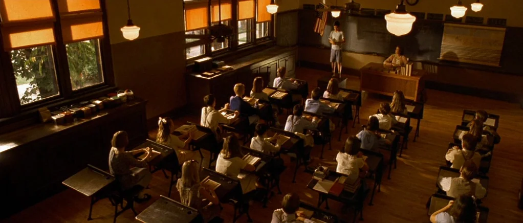 King of the Hill (1993) movie still: wide — An early-to-mid 20th century classroom features rows of wooden desks and a large blackboard. A young…