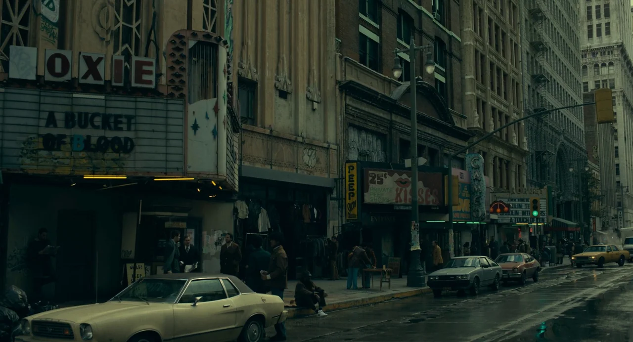 Joker: Folie à Deux (2024) movie still: wide — An urban city street lined with old theaters featuring weathered marquee signs and posters. A small…