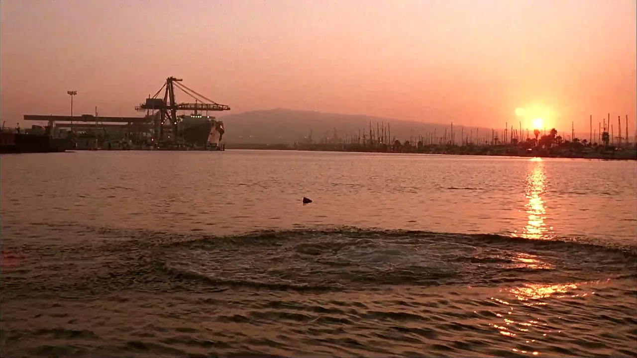 The Mask (1994) movie still: establishing — A harbor at sunset with a large shipping crane and numerous boat masts visible. A noticeable circular…