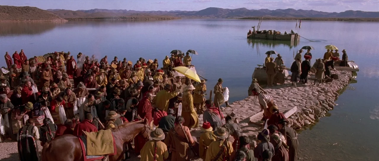 Kundun (1997) movie still: wide — A crowded stone jetty juts into a calm lake surrounded by distant rolling hills. A large group of people in…