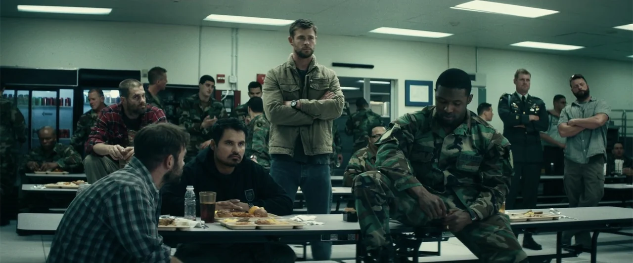 12 Strong (2018) movie still: medium — A utilitarian mess hall features long gray tables and rows of overhead fluorescent lights. Several men in a…