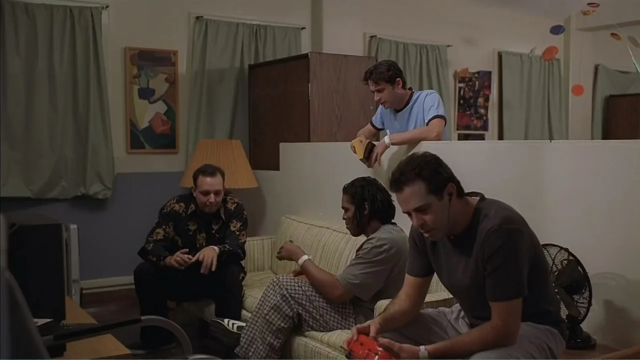 Day of the Dead 2: Contagium (2005) movie still: medium — A spartan common room contains beige walls, curtains, and a striped sofa. Four men sit on…