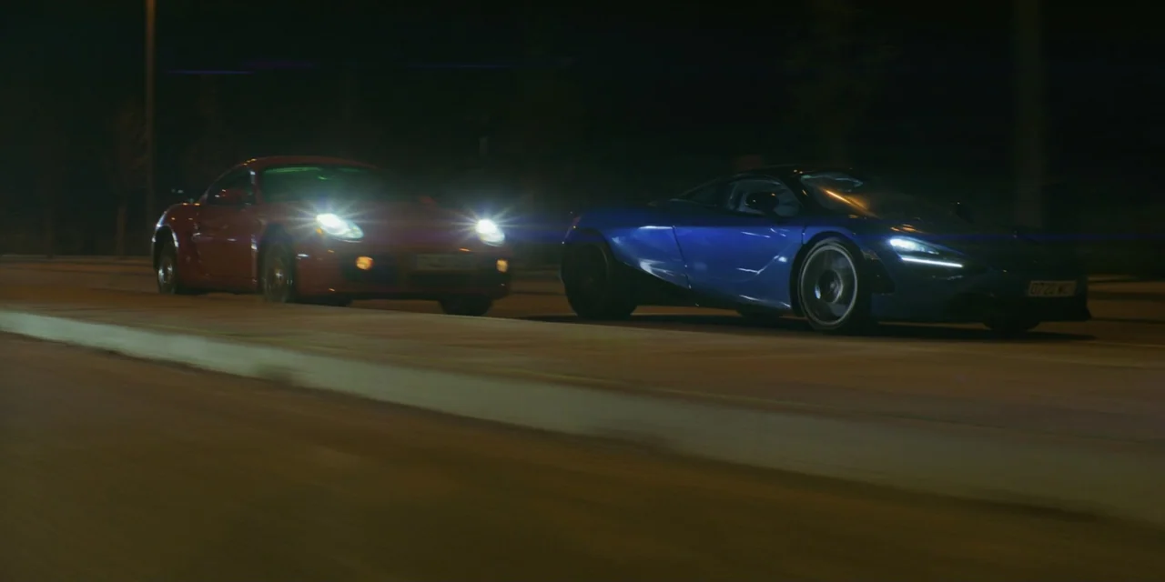 Your Fault (2024) movie still: wide — An empty multi-lane highway at night with dark trees along the roadside. A blue supercar and a red sports car…