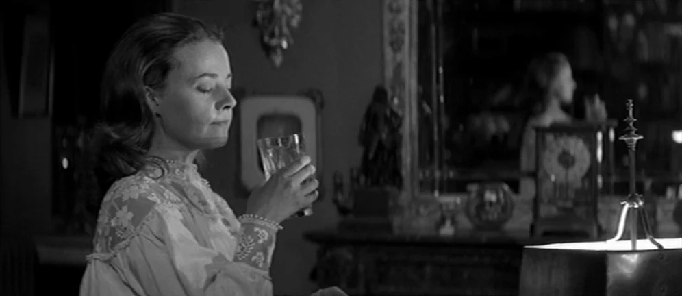 Les Amants (1958) movie still: medium — A dimly lit room contains an ornate fireplace mantel and a reflective surface. A woman in a white lace…