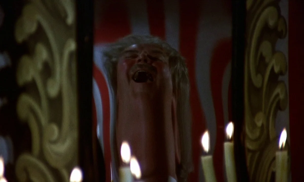 Vampire Circus (1972) movie still: closeup — A distortion mirror in a funhouse reflects the man's head and neck stretched out. The subject laughs…