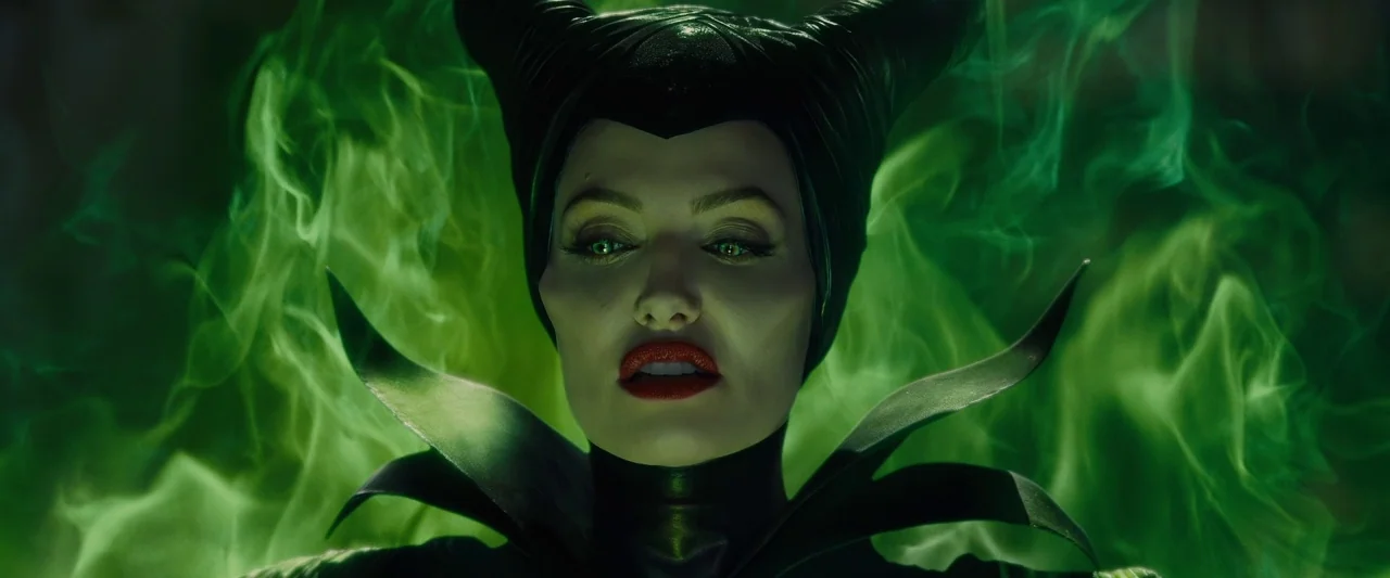 Maleficent (2014) movie still: closeup — A woman with horns stands engulfed in thick, vibrant green magical smoke. She faces forward with a steady…