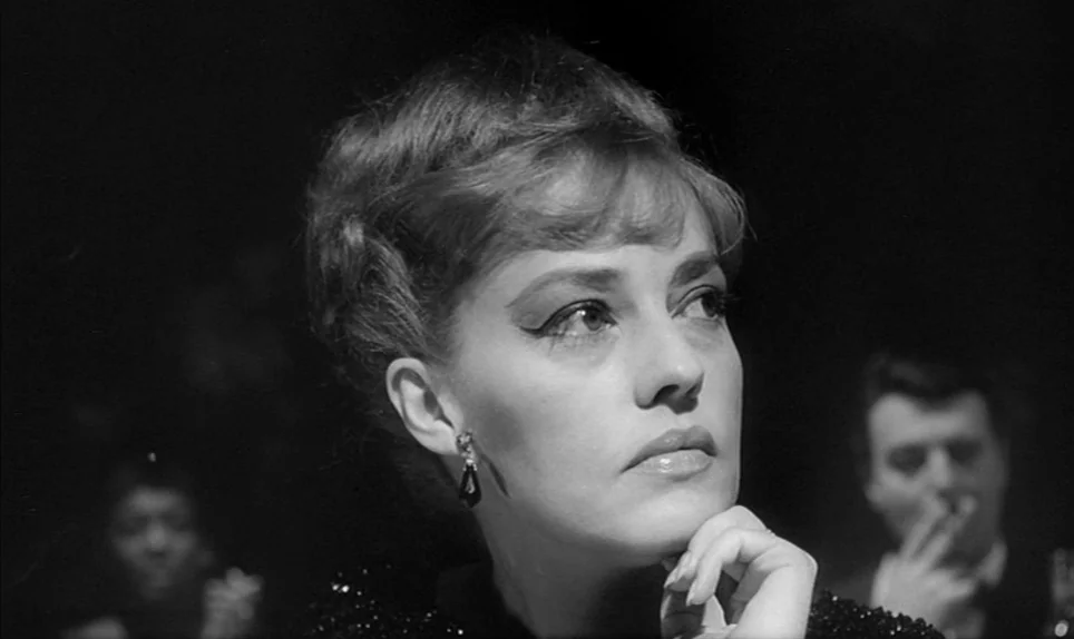 Eva (1962) movie still: closeup — A dark, crowded nightclub setting with soft, focused illumination on the main subject. A woman leans her head on…