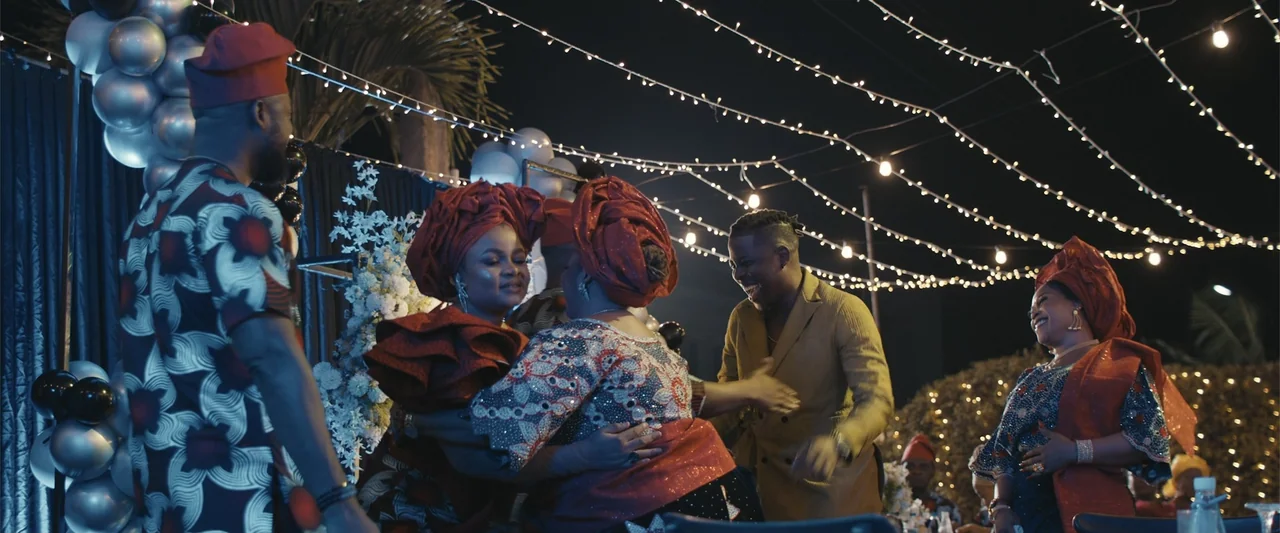 Big Love (2012) movie still: medium — An outdoor evening celebration decorated with string lights and festive balloons at night. Multiple people…