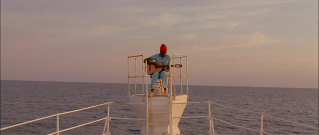 The Life Aquatic With Steve Zissou (2004) movie still: wide — A man sits on a white metal pedestal at the bow of a ship. The vast ocean stretches…