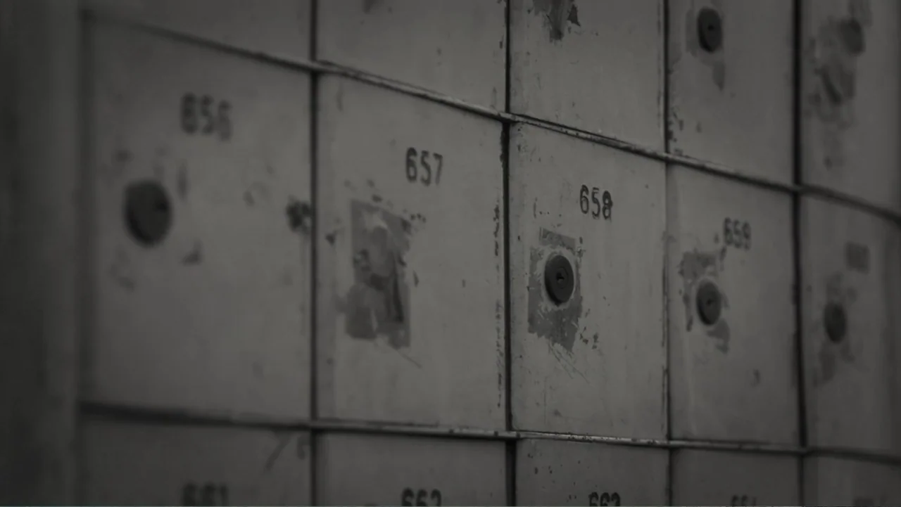 Faya Dayi (2021) movie still: closeup — A close-up view of numbered metal mailboxes arranged in a grid pattern. Each individual mailbox door…