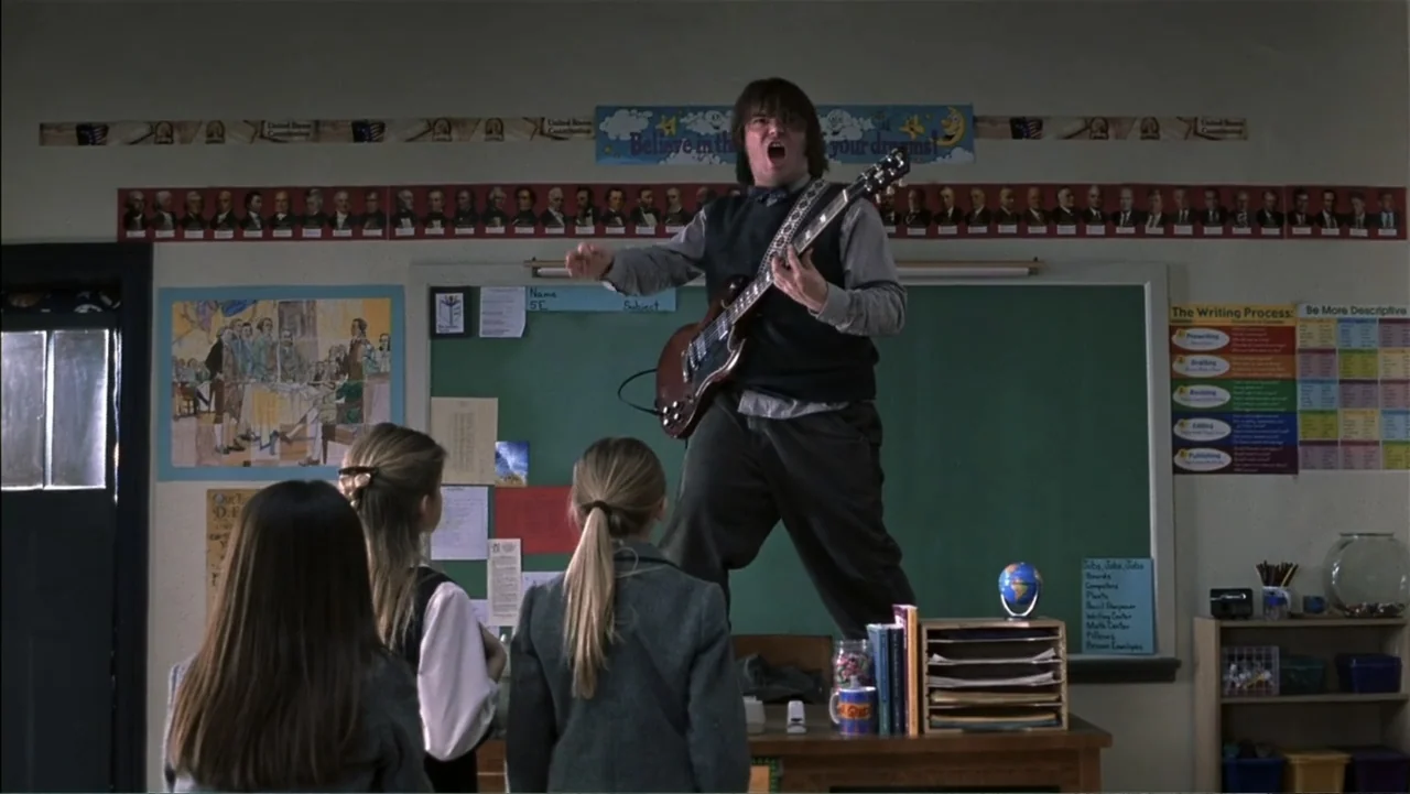 School of Rock (2003) movie still: medium — A school classroom decorated with historical figures and posters on the green chalkboard walls. A man…