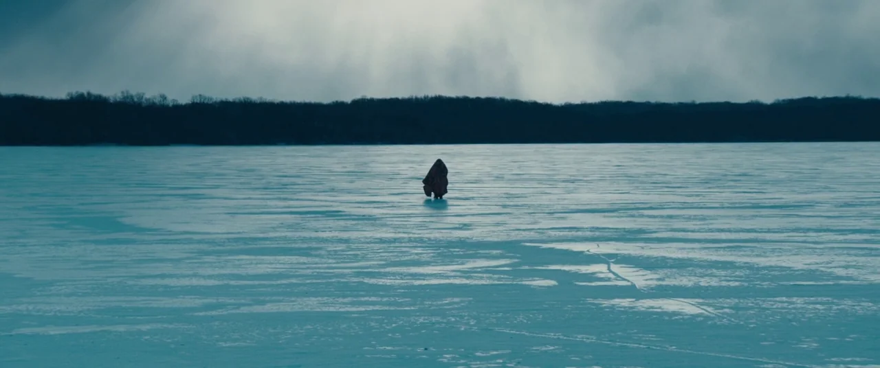 Kumiko the Treasure Hunter (2014) movie still: wide — A vast frozen lake stretches toward a dark, distant treeline under a heavy sky. A single…