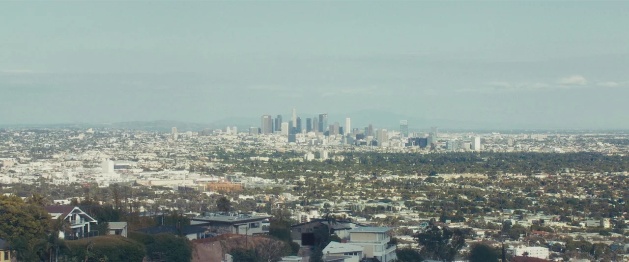 Gemini (2017) movie still: establishing — An aerial panoramic view captures a vast urban sprawl with a dense city skyline. Houses and residential…