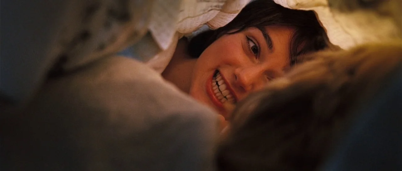 Pride & Prejudice (2005) movie still: closeup — Two people are lying under the covers of a bed in a dark room. The woman smiles while looking at the…