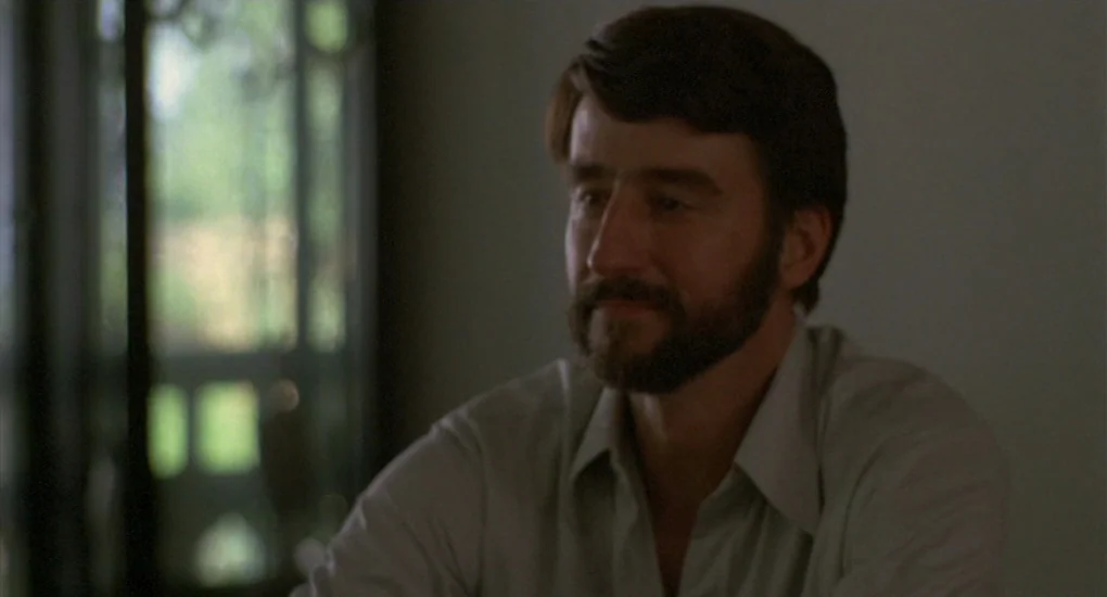 The Killing Fields (1984) movie still: medium — A man with a beard sits inside a room near a window. He looks toward the side of the frame.