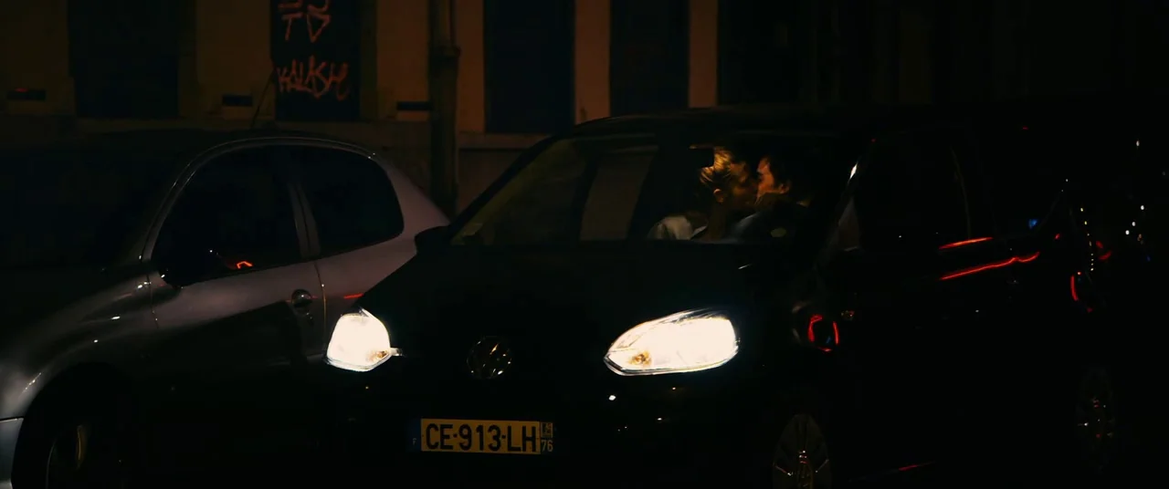 Blue Is The Warmest Colour (2013) movie still: medium — A dark night scene shows two cars parked along a city wall with graffiti. A couple sits in…