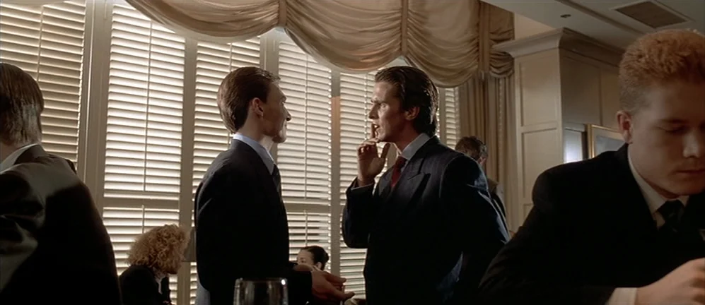 American Psycho (2000) movie still: medium — A bright indoor space features floor-to-ceiling windows covered by horizontal white wooden blinds. Two…