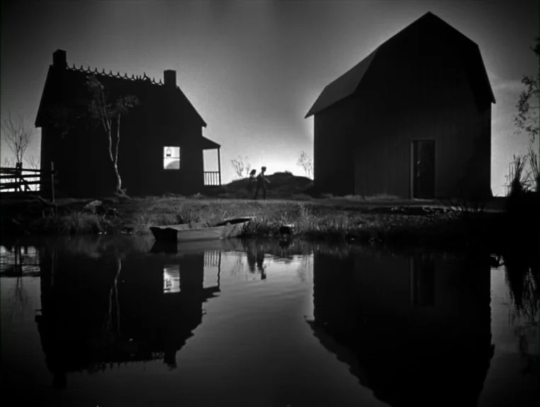 The Night Of The Hunter (1955) movie still: wide — A dark farmstead with a house and barn stands silhouetted against a setting sun. The structures…
