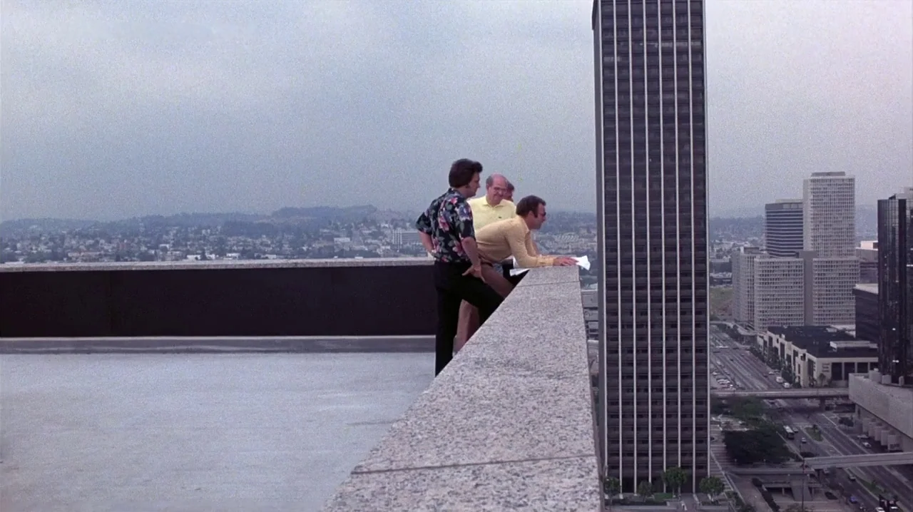 Thief (1981) movie still: wide — A high-rise building rooftop overlooking a sprawling urban landscape under a cloudy sky. Three men stand by the…