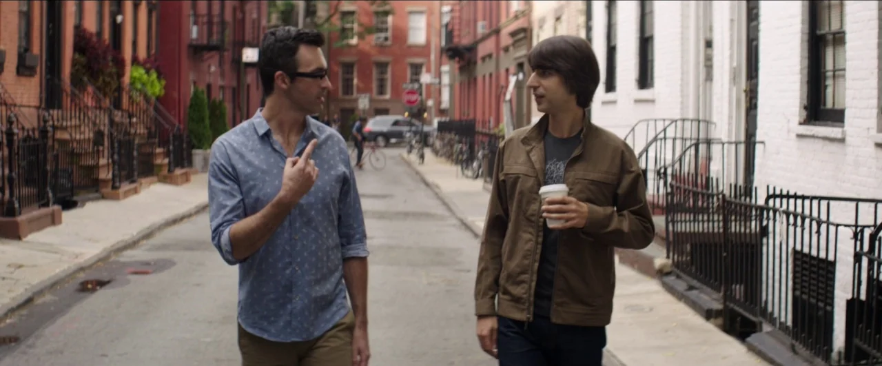 Dean (2016) movie still: fullbody — A quiet residential street in a city with brownstone buildings on both sides. Two men walk down the center of…